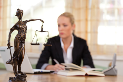 Das Bild zeigt eine Referendarin am Schreibtisch beim Studium und auf dem Tisch im Vordergrund die Justitia (die Personifikation der Gerechtigkeit) ist das Symbol der Gerichtsbarkeit. Ihre Waage ist ein Sinnbild für das Abwägen von Standpunkten und das Zumessen der Strafe. Ihr Buch symbolisiert das Gesetz und das Schwert dessen Durchsetzung.